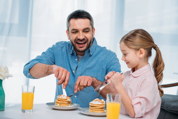 cheerful father and little daughter having breakfast at home - Foto, Bild
