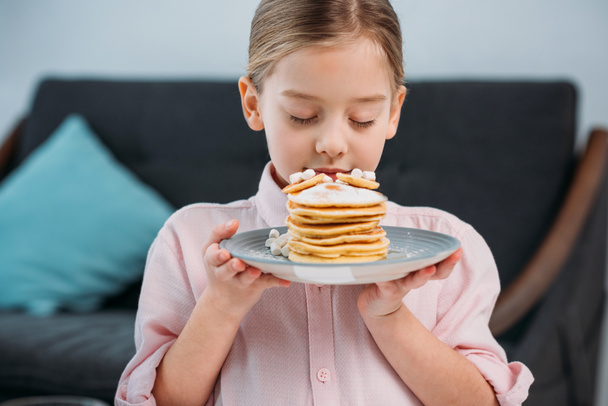 portrait of kid sniffing homemade pancakes on plate for breakfast in hands - Fotoğraf, Görsel