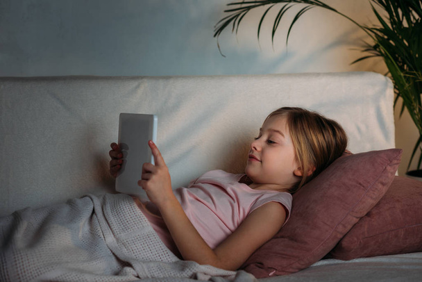 side view of little kid using tablet in bed at home - Photo, Image