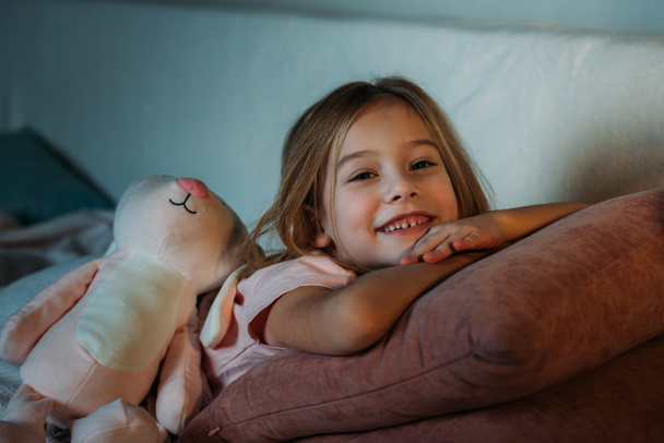 portrait of smiling kid with toy lying on sofa - Foto, afbeelding
