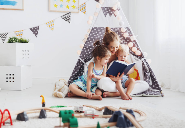 perheen äiti lukemassa lapsille varata teltassa kotona - Valokuva, kuva