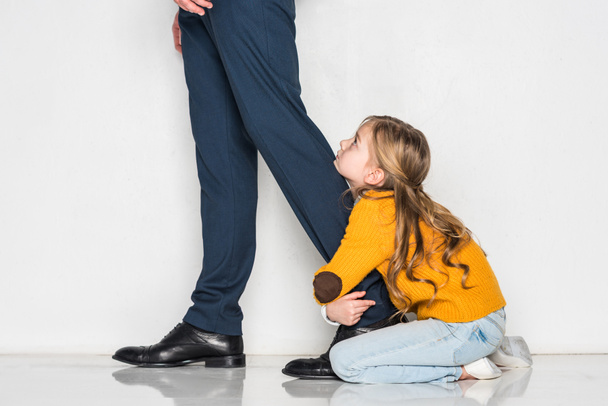 Kleine Tochter umarmt Vater im Business-Anzug isoliert auf grauem, einsamem Konzept - Foto, Bild