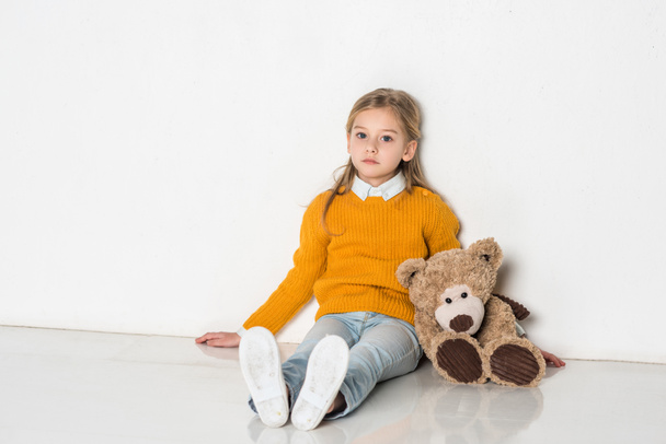 little kid with teddy bear looking at camera while sitting on floor - Fotoğraf, Görsel