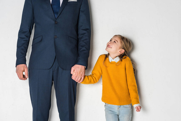 partial view of sad daughter and father in business suit holding hands isolated on grey - Fotografie, Obrázek
