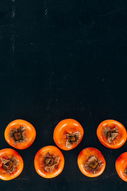 top view of persimmons in rows on black - Fotografie, Obrázek