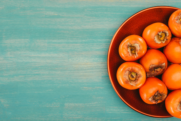top view of persimmons on red plate on turquoise table - Photo, Image