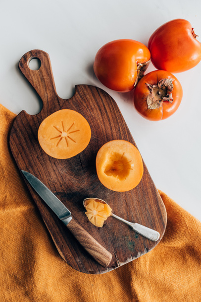 top view of persimmons on wooden board with knife and spoon - Fotografie, Obrázek