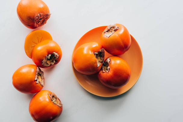 top view of persimmons on orange plate and on white tabletop - Zdjęcie, obraz