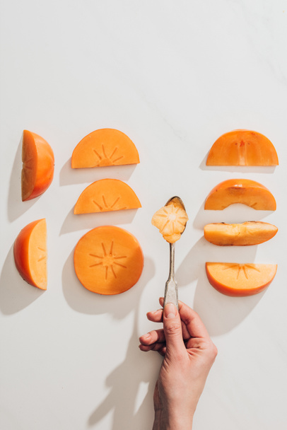 cropped image of woman holding spoon above persimmon pieces  - Photo, Image