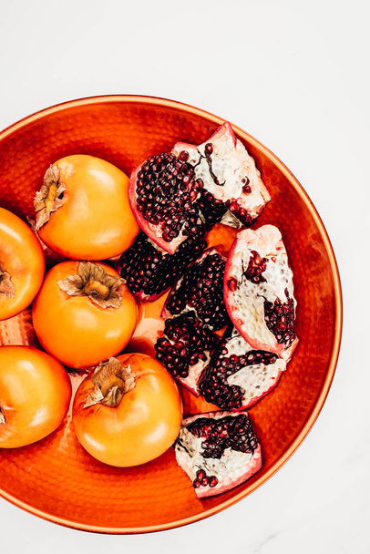 elevated view of persimmons and pomegranates on red plate isolated on white - 写真・画像