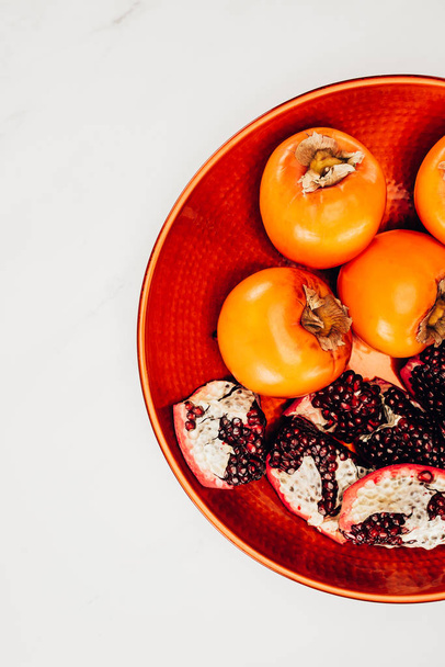 top view of persimmons and pomegranates on red plate isolated on white - Photo, Image