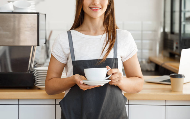 Coffee Business Concept - Caucasian female serving coffee while standing in coffee shop. Focus on female hands placing a cup of coffee. - Photo, Image
