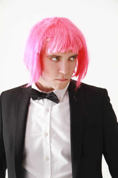 stylish and funny young guy standing in business suit and pink women wig on white background alone - Photo, Image
