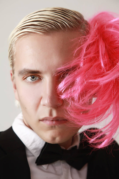 stylische und lustige junge Mann steht in Business-Anzug und rosa Frauen Perücke auf weißem Hintergrund allein - Foto, Bild