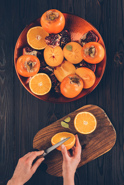 περικομμένη εικόνα γυναίκα κοπής πορτοκαλιού σε ξύλινη σανίδα - Φωτογραφία, εικόνα
