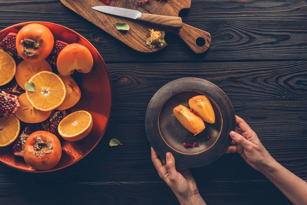 cropped image of woman holding plate with persimmon pieces - Foto, Imagem
