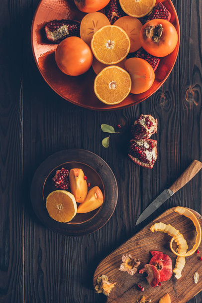 elevated view of persimmons with oranges and pomegranates on plates - 写真・画像