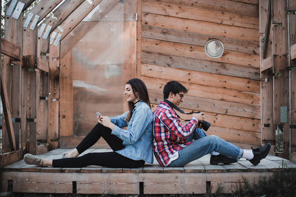 young man and woman sitting against wooden background  man holding camera - Fotografie, Obrázek