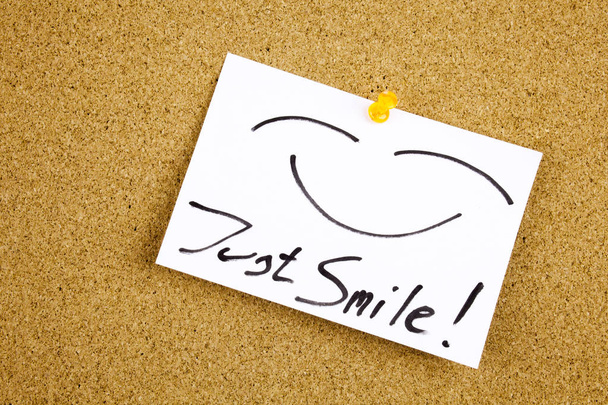 Una nota adhesiva amarilla escritura, leyenda, inscripción Vista superior de la nota adhesiva Just Smile pegada en texto negro en una nota adhesiva fijada a un tablón de anuncios de corcho
 - Foto, Imagen