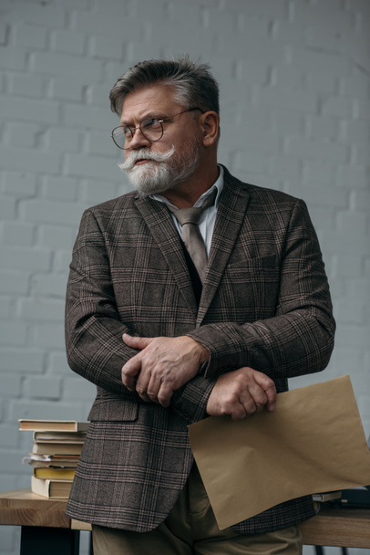 senior man with sheet of kraft paper looking away at workplace - Fotoğraf, Görsel