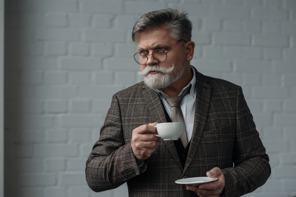 hombre mayor guapo con taza de café delante de la pared de ladrillo blanco
 - Foto, imagen