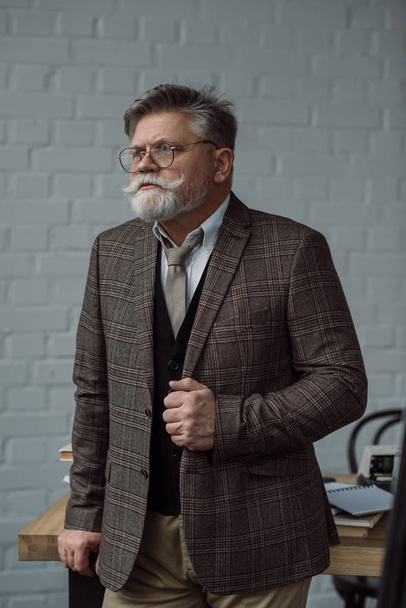 Ανώτερος συγγραφέας στο κοστούμι tweed και γυαλιά κοντά στο χώρο εργασίας - Φωτογραφία, εικόνα