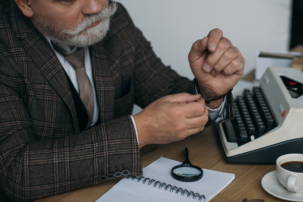 περικοπεί shot ανώτερος συγγραφέας βάζοντας σε vintage ρολόι του στο χώρο εργασίας - Φωτογραφία, εικόνα