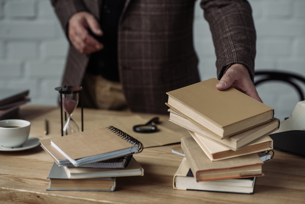 обрізаний знімок людини, що бере стопки книг зі столу
 - Фото, зображення