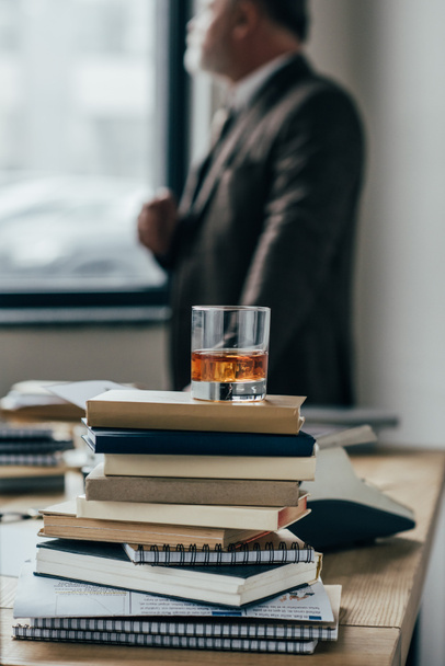 primer plano de vaso de whisky en la pila de libros con el hombre mayor de pie borrosa sobre el fondo
 - Foto, Imagen