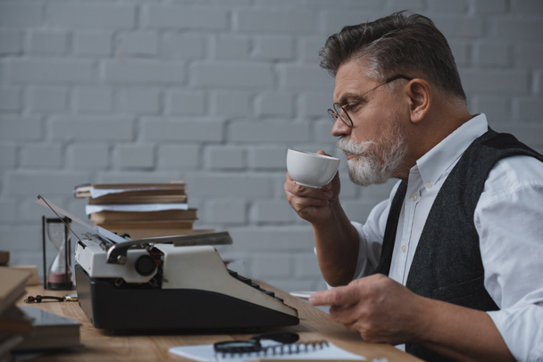 escritor sênior trabalhando com máquina de escrever vintage e beber café
 - Foto, Imagem