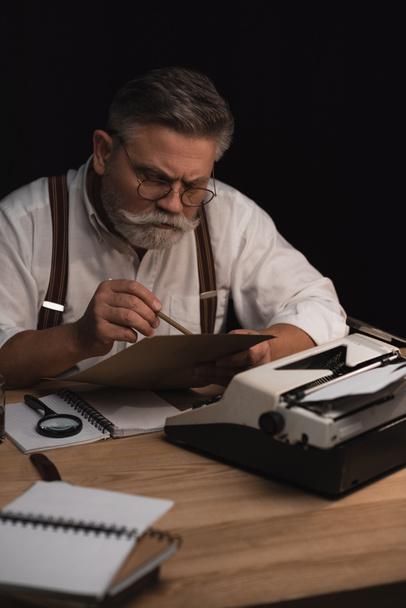 escritor senior enfocado trabajando con manuscrito aislado en negro
 - Foto, imagen