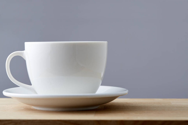 Selective focus side close up view white teacup and saucer isolated on grey background - Фото, изображение