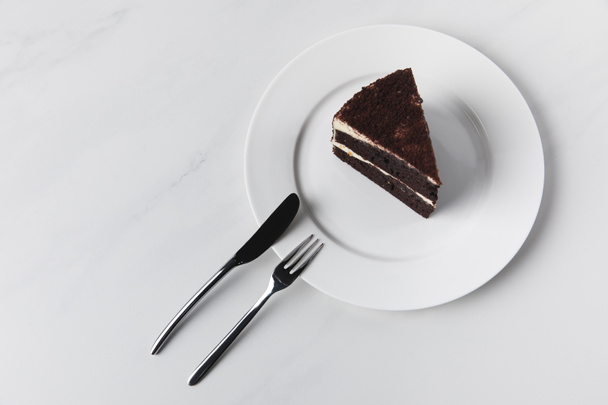 Шоколадный торт на тарелке с вилкой и ножом на белой поверхности
 - Фото, изображение