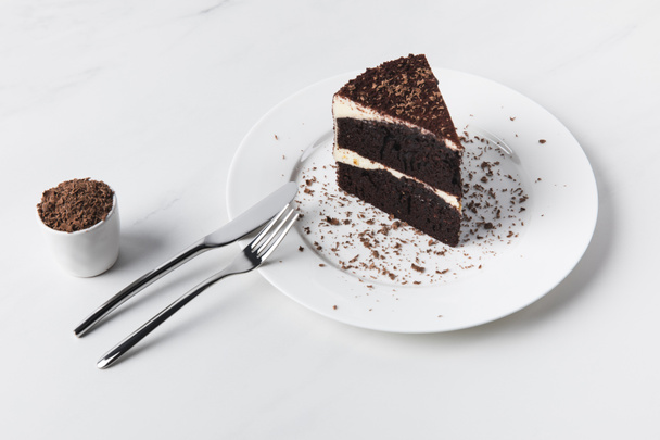 Grated chocolate in bowl, cutlery and cake on plate  - Foto, Bild