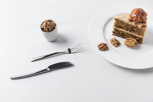 Μαχαιροπίρουνα και πλάκα με κέικ τοποθετούνται σε λευκή επιφάνεια - Φωτογραφία, εικόνα