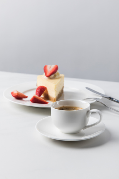 Cheesecake with strawberries on plate and cup of coffee on foreground - Photo, Image