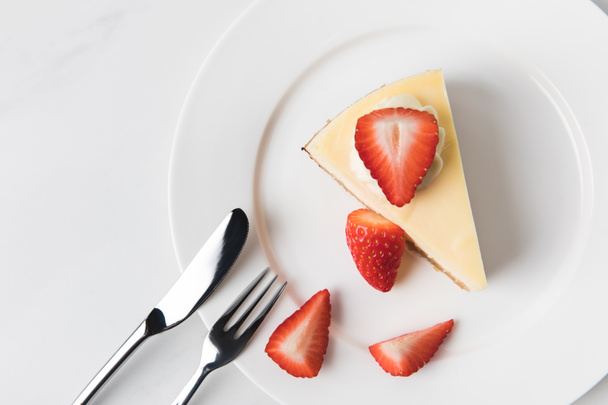 Plate with cheesecake surrounding by sliced strawberries  - Фото, изображение