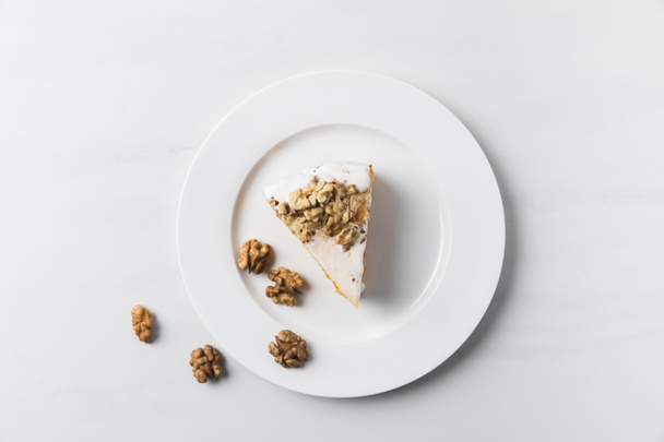Plate with cake surrounding by walnuts placed on white surface  - Fotografie, Obrázek
