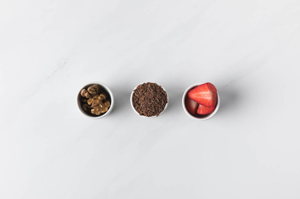 Three bowls with walnuts, grated chocolate and strawberries on white - Φωτογραφία, εικόνα