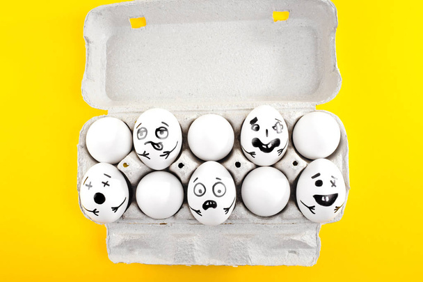 Пасхальні яйця з намальованими мультяшними обличчями в картонному лотку на жовтому фоні
. - Фото, зображення