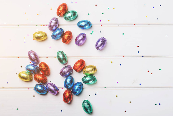 Velikonoční čokoládové mini vejce zabalená v barevné fólie, roztroušených na bílé dřevěné pozadí, pohled shora, kopie prostor. - Fotografie, Obrázek