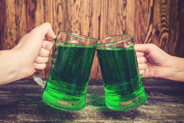 Friends, holding two mug of green beer against wooden wall. - Photo, Image
