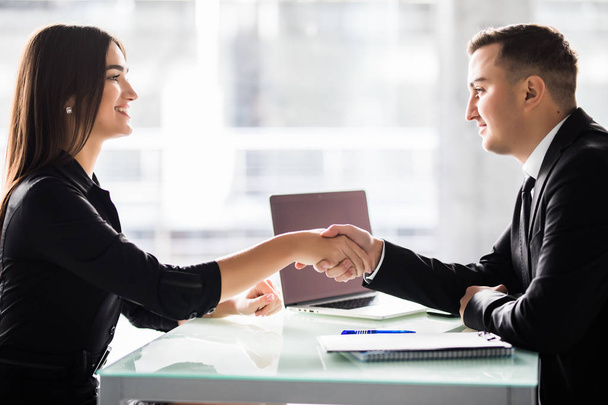 Businesswoman and businessman shaking hands over the table with laptop and papers at the office, pleasant business meeting, starting negotiation. - Foto, Imagen