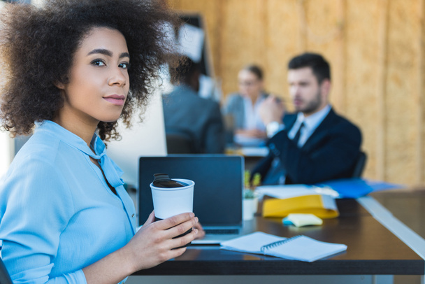 Afrikanisch-amerikanische Geschäftsfrau hält eine Tasse Kaffee in der Hand und blickt in die Kamera im Büro - Foto, Bild