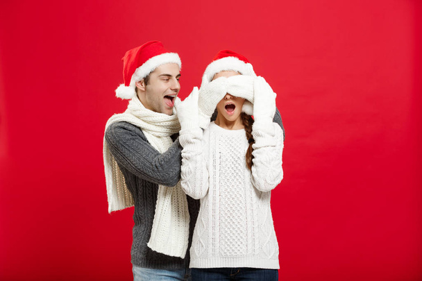 Christmas concept - Portrait of a romantic young boyfriend surprising girlfriend over red studio background. - Photo, Image
