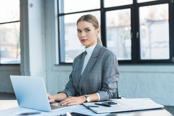 beautiful businesswoman using laptop in office and looking at camera - Foto, Bild