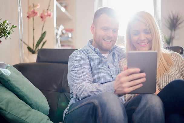 Couple utilisant la tablette tout en étant assis sur le canapé à la maison
. - Photo, image