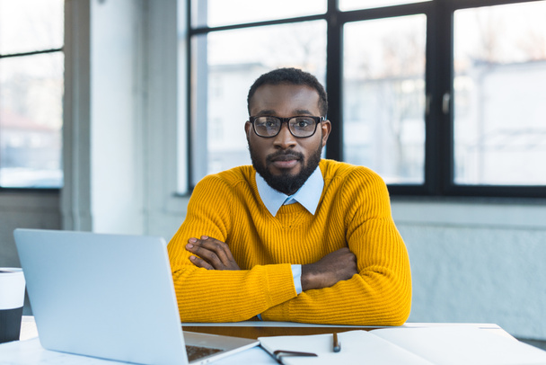 Αφρικανικός Αμερικανός επιχειρηματίας, κάθονται με σταυρωμένα τα χέρια και κοιτάζοντας κάμερα στο γραφείο - Φωτογραφία, εικόνα
