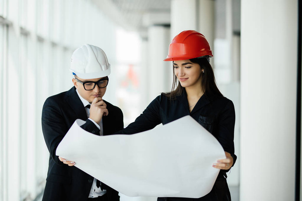 Biznesmen architektów spojrzeć na papier plan biznes kobieta architekt w biurze do omówienia projektów biznesowych w pobliżu panoramiczne okna. - Zdjęcie, obraz