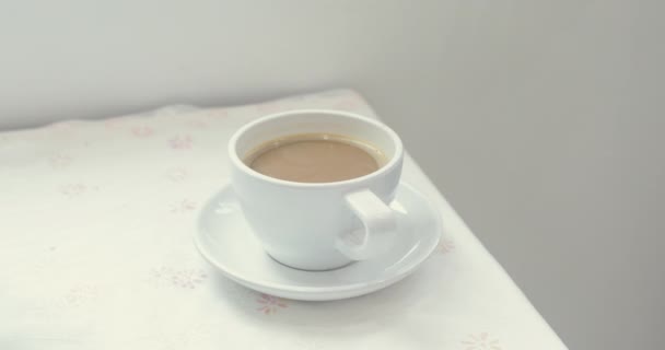 Vértes Nézd női kéz vesz egy fehér csésze forró kávét a táblából. Majd kamera mozog egy csésze, és ez a nő kezd inni a kávét. - Felvétel, videó